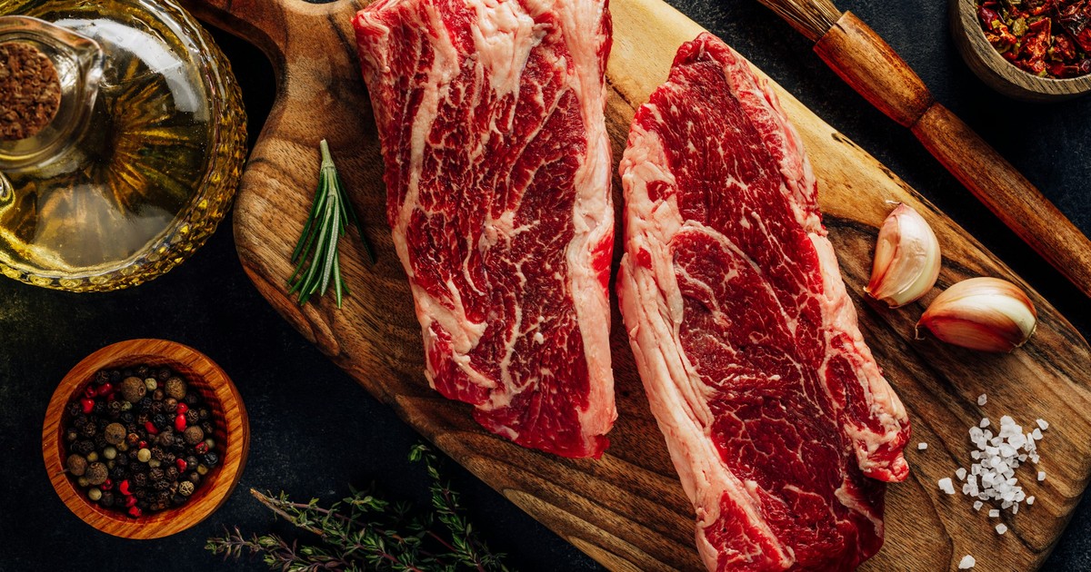 Pièces de bœuf cru sur une planche avec ail, poivre et herbes
